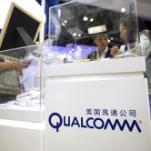 Conference visitors look at a display booth for Qualcomm.