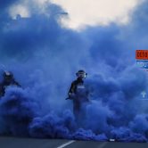 Minneapolis police in riot gear walk through a cloud of blue smoke