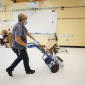 A custodian moves chairs out of a school classroom