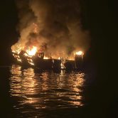A dive boat is engulfed in flames on the water at nighttime