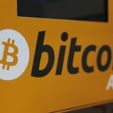 The Bitcoin logo appears in black against a yellow background on an ATM.