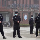 Four security personnel stand outside the entrance of the Wuhan Institute of Virology.