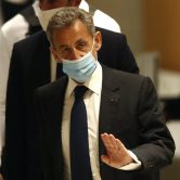 Masked Nicolas Sarkozy walks into court.