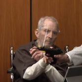 Robert Durst holding a pistol on the witness stand during his murder trial.