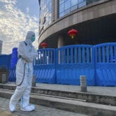 A worker in protective overalls and disinfecting equipment walks outside a Wuhan Hospital.