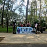 a group of six people stand next to a poster that says "Justice for R. Kelly, due process, one man ain't no enterprise"