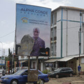 People walk past a defaced billboard with former Guinea President Alpha Conde.