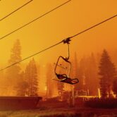 This photo shows the chair of a ski lift in the foreground with a forest fire raging behind.