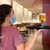 Server with face mask carrying a glass of beer