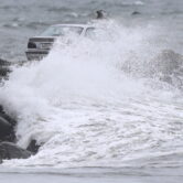 A car is covered by a large wave as a nor'easter makes its way across the Northeast.