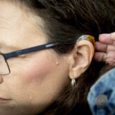 A woman brushes her hair away from her hearing aid.