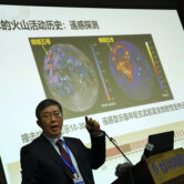 Li Xianhua speaks near a screen showing volcanic activities on the moon