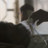 An Indian relative adjusts the oxygen mask of a patient suffering from tuberculosis.