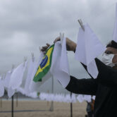 An activist holds the Brazilian national flag in the middle of a clothesline with white scarves representing Covid-19 victims.
