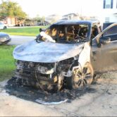 a charred SUV with its font fender destroyed parked in a driveway