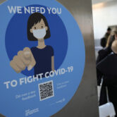 A woman wearing a face mask walks past a Covid-19 awareness sign.