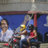 A motorcyclist rides past a mural of Daniel Ortega and Cesar Augusto Sandino in Nicaragua.