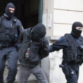 Police officers lead a suspect out of a building during a raid in Germany.