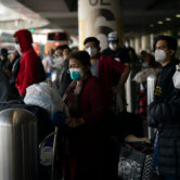 Masked travelers wait for a shuttle bus to arrive at the Los Angeles International Airport