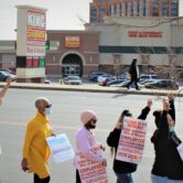 People with picket signs walk past a King Sooper grocery store sign