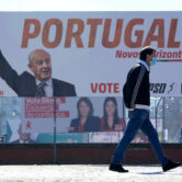 A man wearing a face mask walks past election campaign billboards in Portugal.