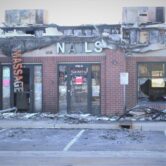 Burned brick building, broken plate glass windows, destroyed signage.