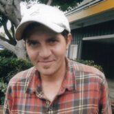 Photo of a man wearing a ball cap and flannel.