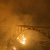 Wildfire burns beneath an open-spandrel arch bridge.