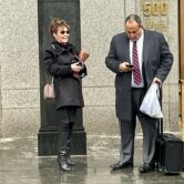 Sarah Palin is standing outside the courthouse at 500 Pearl Street laughing, next to her attorney who is on his phone