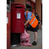 A postman empties a mailbox in London