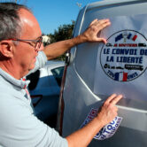 A man puts a poster that reads "Liberty Convoy" on a van in France.