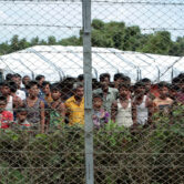 Rohingya refugees gather near a fence on land between Myanmar and Bangladesh.