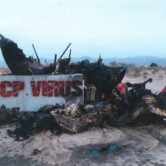 in the foreground is a sign that said CCP VIRUS in front of a burned pile of materials, with mountains in the background