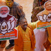 A BJP worker displays party symbol with photos of Narendra Modi and Yogi Adityanath.