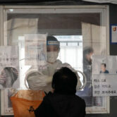 A medical worker in a booth takes a nasal swab sample from a woman in South Korea.