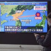 A woman walks past a TV showing a news program's coverage of a North Korean missile launch.