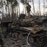 A Ukrainian soldier stands on a destroyed Russian tank