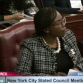 NYC Councilmember Natansha Williams sits at a council meeting in a maroon leather chair, a stripe at the bottom reads New York City Stated Council Meeting with the date 4/28/2022