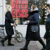 People walk past a currency exchange office screen in Moscow, Russia.