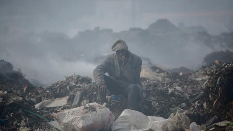 A recycling scavenger smokes a cigarette on a mountain of garbage in Kenya.