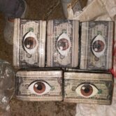 five packages of cocaine wrapped in plastic wrap are laid out, each one has a dollar bill wrapped around the outside of the brick and a brown eye emoji image on the package