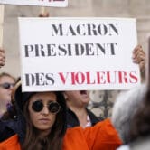 Woman holds a poster reading "Macron, President of rapists" during a demonstration in Paris.