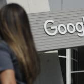 A woman walks below a Google sign on its campus in Mountain View, Calif.