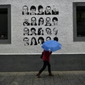 A woman shelters from the rain under an umbrella while walking past portraits of ETA prisoners.