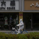 A worker in a protective suit rides a bicycle past shuttered retail shops in Beijing.