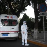 A worker wearing a protective suit stands outside an ambulance in Beijing.