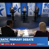 a screenshot of a televised debate for New York governor shows Governor Kathy Hochul at a podium in the middle. To the left is NYC Public Advocate Jumaane Williams and to the right is Representative Tom Suozzi