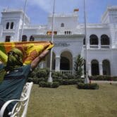 A protester holds the Sri Lankan flag while sitting in a chair on a lawn.