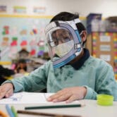 A student wears a mask and face shield in a 4th grade class.