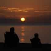 A pair of beachgoers watch the sun rise over the Atlantic Ocean.